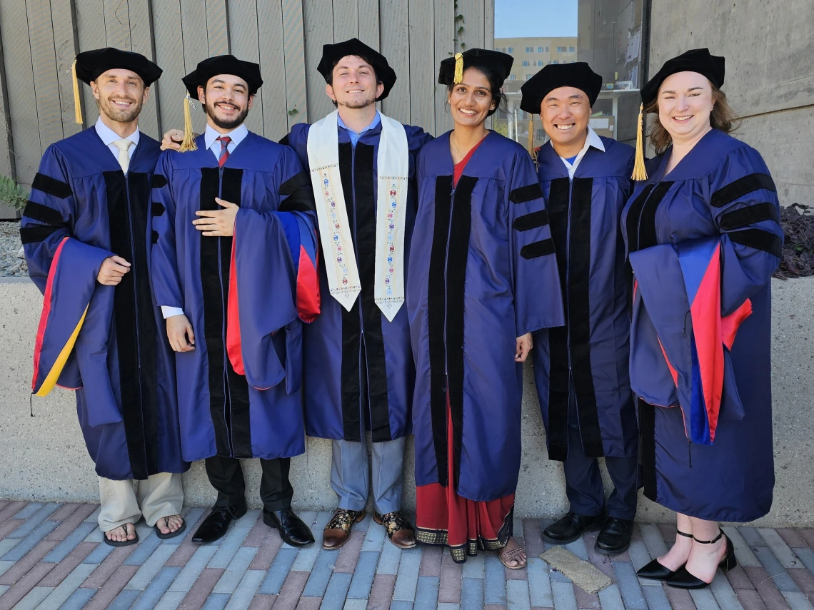 Six PhD students in caps and gowns celebrate graduation